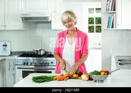 Légumes frais assis sur une planche à découper en bois au comptoir de cuisine blanc, gamme en acier inoxydable Banque D'Images