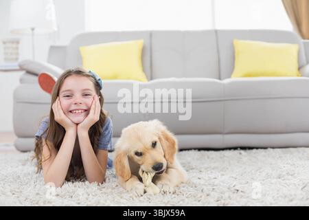 Fille enfant couché sur le tapis de salon souriant tandis que chiot jouet corde à mâcher, espace de copie Banque D'Images