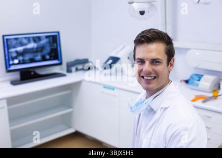 Dentiste masculin debout près du comptoir dans la salle de traitement avec radiographie dentaire sur le moniteur, espace de copie Banque D'Images