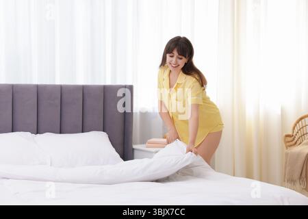 Belle jeune femme faisant lit à la maison Banque D'Images