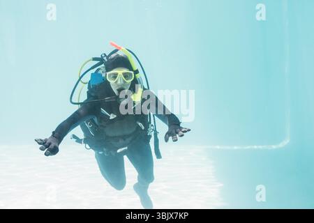 Plongeur sous-marin pratiquant sous l'eau dans une piscine claire, portant l'équipement complet et un masque jaune près du sol carrelé Banque D'Images
