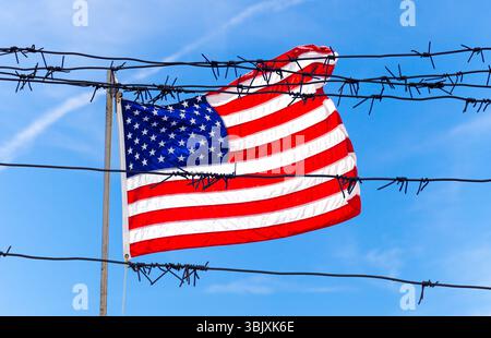 Clôture barbelée en fil métallique devant le drapeau des États-Unis d'Amérique qui agite dans le vent Banque D'Images
