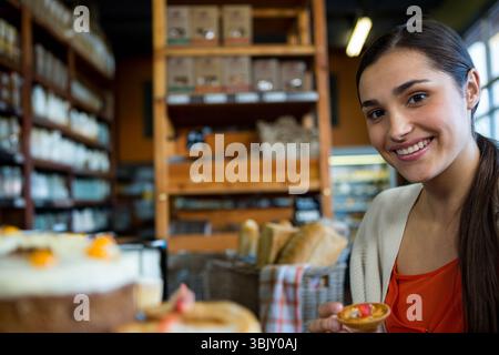 Femme souriante et tenant une petite tarte aux fruits dans la boulangerie avec des pâtisseries et des paniers à pain, espace copie Banque D'Images