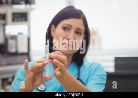Infirmière adulte portant des gommages, stéthoscope debout dans la salle de clinique aspirant le liquide dans la seringue Banque D'Images