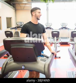 Les tapis roulants sont debout sur le sol en caoutchouc rouge dans l'intérieur lumineux de la salle de gym, avec la plante en pot suspendue Banque D'Images