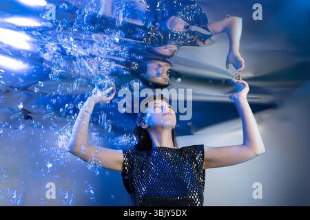 Une fille habillée comme une sirène capte l'attention tout en étant submergée dans l'eau claire. Des bulles l'entourent, ajoutant à l'ambiance fantastique du monde sous-marin qu'elle habite. Banque D'Images
