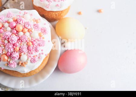 Pain ou gâteaux sucrés traditionnels de Pâques avec glaçage blanc et décor de sucre, œufs colorés et branche de cerisier en fleur sur blanc Banque D'Images