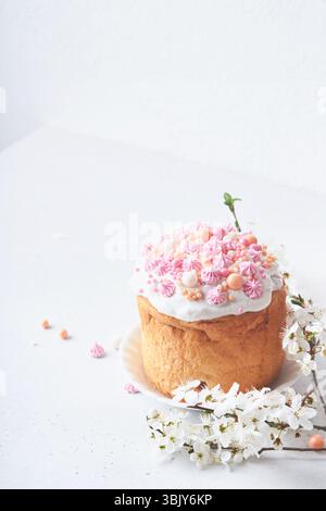 Pain ou gâteaux sucrés traditionnels de Pâques avec glaçage blanc et décor de sucre, œufs colorés et branche de cerisier en fleur sur blanc Banque D'Images