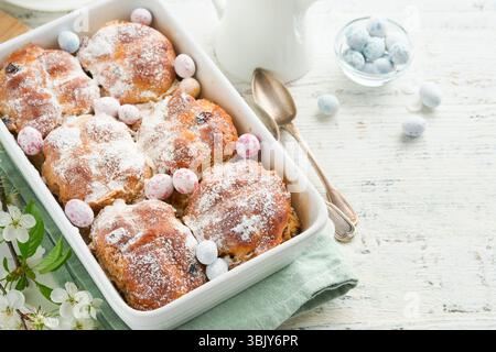 Pains croisés chauds de Pâques. Les gâteries traditionnelles de Pâques croisent les petits pains aux raisins secs, le beurre, les œufs de bonbons au chocolat avec la cerise florissante ou Banque D'Images