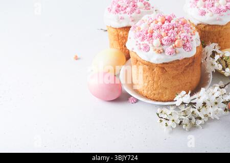 Pain ou gâteaux sucrés traditionnels de Pâques avec glaçage blanc et décor de sucre, œufs colorés et branche de cerisier en fleur sur blanc Banque D'Images