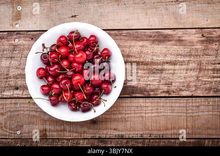 Cerise avec des gouttes d'eau sur un bol blanc sur une table en pierre brun foncé. Cerises fraîches mûres. Cerises rouges douces. Vue de dessus. Style rustique Banque D'Images