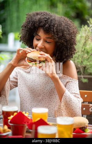 Jeune femme dégustant un hamburger dans un restaurant avec de la bière et des frites Banque D'Images