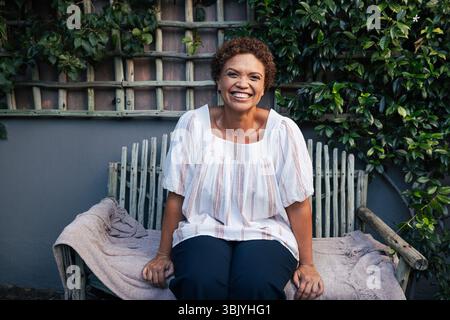 Bonne femme mûre sur un banc. Femme souriante aux cheveux courts se détendant dans l'arrière-cour. Banque D'Images