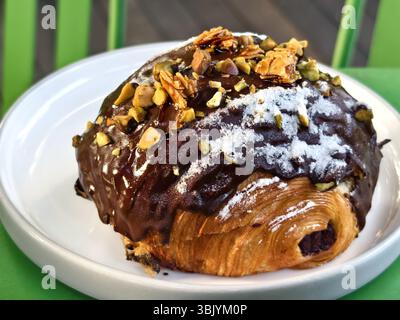 Croissant au beurre recouvert de glaçage au chocolat, recouvert de poussière de sucre, de pistaches et de friabilité aux amandes Banque D'Images