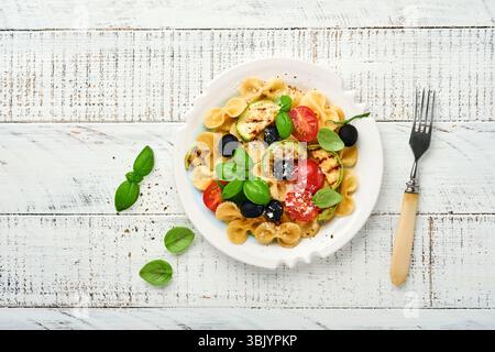 Salade de pâtes fiocchi avec légumes courgettes grillées, tomates cerises, olives, basilic et fromage parmesan dans une assiette blanche sur lumière s. Banque D'Images