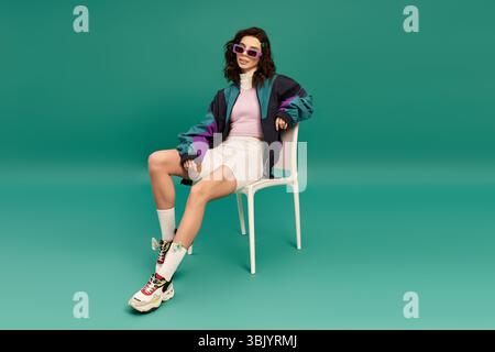 Jeune femme présente un style sportif avant-gardiste sur un fond turquoise vibrant à l'intérieur. Banque D'Images