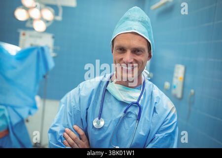 Chirurgien masculin adulte moyen portant des gommages croisant les bras OU une table sous OU des lumières avec stéthoscope Banque D'Images