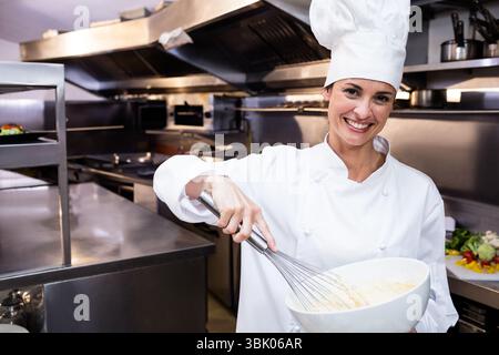 Fouet métallique fouettant la pâte crémeuse dans un grand bol blanc sur le poste de travail en acier dans la cuisine commerciale Banque D'Images