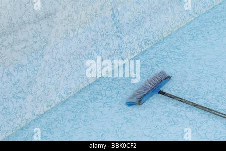 Nettoyage privé de la piscine avec brosse à long manche ; piscine vide de la cour arrière en cours de nettoyage. Banque D'Images