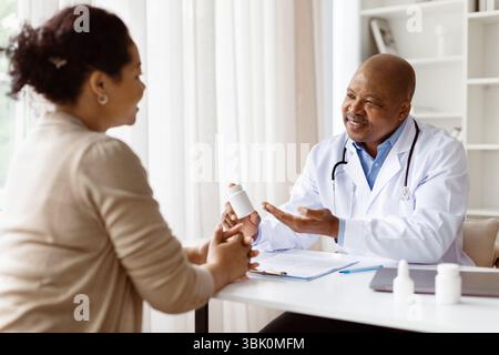Prescription pharmaceutique. Docteur masculin mature montrant la bouteille de pilules au patient féminin Banque D'Images