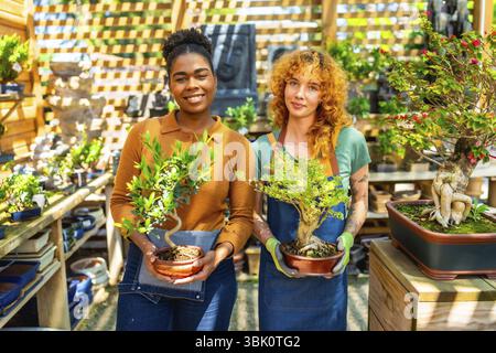 Deux femmes jardinières tenant et prenant soin des bonsaï tout en travaillant ensemble dans une pépinière de plantes ou un centre de jardin dynamique Banque D'Images