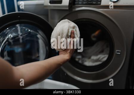 Femme de ménage plaçant des serviettes blanches dans la machine à laver, se préparant pour le cycle de lavage dans la buanderie moderne, gros plan. Banque D'Images