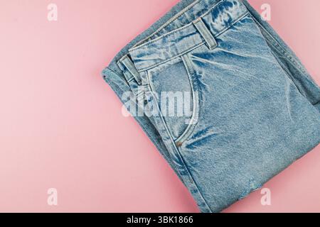 Les jeans denim sont soigneusement pliés et placés sur une surface rose douce, mettant en valeur leur couleur bleu clair et leur style décontracté. Idéal pour les passionnés de mode. Banque D'Images