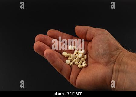 Une main est ouverte et étendue, montrant plusieurs petites tablettes blanches posées dans la paume, avec un fond sombre créant un effet contrastant. Banque D'Images