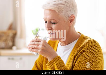 Belle femme âgée ayant un verre d'eau à la maison Banque D'Images