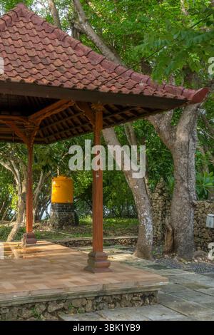 Petit pavillon avec une cloche suspendue au toit. Le pavillon est entouré d'arbres et a un mur de pierre en arrière-plan Banque D'Images