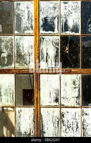 Les vitres fissurées et qui se décollent reflètent la lumière et les objets voisins, créant une atmosphère de nostalgie dans un intérieur vieilli Banque D'Images