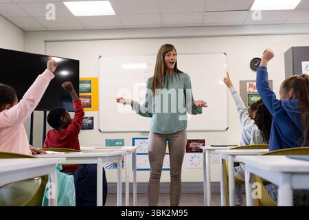 Enseignante s'engageant avec des élèves enthousiastes et divers levant la main en classe, à l'école Banque D'Images