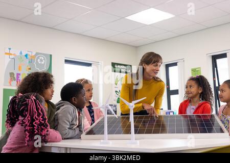 Enseignante attirant divers élèves avec des panneaux solaires dans une salle de classe écologique, à l'école Banque D'Images
