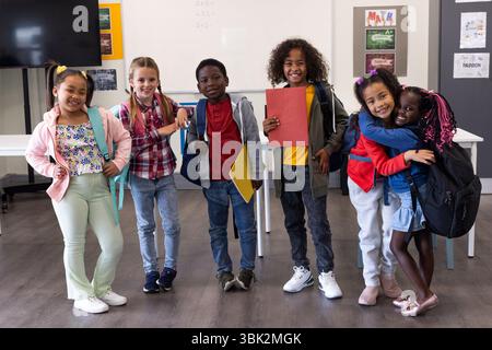À l'école, souriant des enfants divers avec des sacs à dos en classe, prêts pour l'apprentissage Banque D'Images