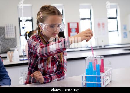 Fille dans le laboratoire de l'école menant des expériences avec des éprouvettes, portant des lunettes de sécurité Banque D'Images
