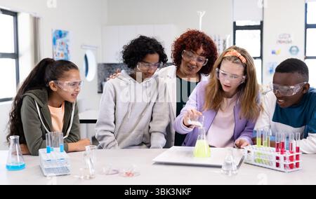 À l'école, divers élèves portant des lunettes de sécurité conduisant des expériences scientifiques avec une enseignante Banque D'Images