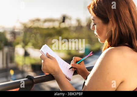 Un gros plan intime d'une jeune femme écrivant dans son journal à l'extérieur. Concept d'écriture créative, d'étude, de planification ou de pleine conscience Banque D'Images