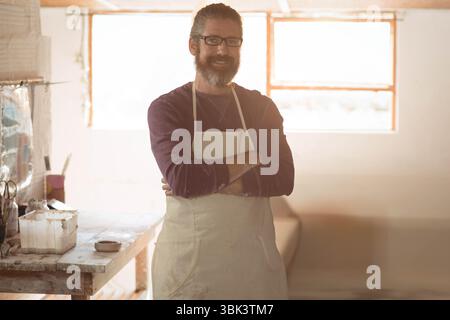 Homme adulte artisan debout à l'atelier portant tablier teinté mélangeant la peinture dans un bol sur l'établi Banque D'Images