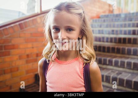 Sac à dos violet reposant sur un escalier en brique avec main courante en métal et lumière du jour à l'entrée de l'école Banque D'Images