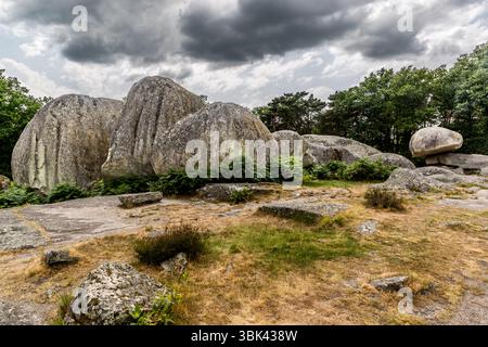Les blocs de granit des Pierres Jaumâtres, un monument naturel, se trouvent sur le Mont Barlot (591 mètres) près de Toulx-Sainte-Croix, dans le département de la Creuse, Nouvelle-Aquitaine, France. De gros rochers arrondis sont serrés les uns contre les autres, et sur la droite, un bloc repose sur un rocher plus plat. Des fougères et de la bruyère poussent entre les pierres, et des dalles de granit plates, des pierres et de l'herbe sèche gisent au premier plan. Des nuages sombres traversent le ciel. Il s'agit d'une collection d'environ 40 roches de granit massives formées par l'érosion et entourées de légendes et de croyances mystiques depuis des siècles. L'altération et l'érosion ont modelé les blocs pendant le Quaternaire. Banque D'Images
