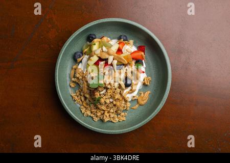 Un bol de petit-déjeuner coloré comprend du yaourt, des fruits frais, du granola et du beurre de noix, parfait pour un repas matinal nutritif. Banque D'Images