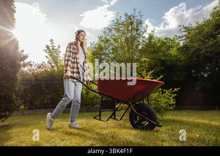 Jardinière féminine travaillant en automne, coupant l'herbe dans la cour arrière. Concept de jardinage, travail, nature. Travaux ménagers, jardinage et vie à la campagne. Jardin de la maison. Banque D'Images