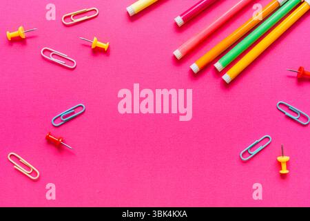 Stylos aux couleurs vives, trombones et punaises disposés sur un fond rose vif. Concept de retour à l'école dans le style pop art. Banque D'Images