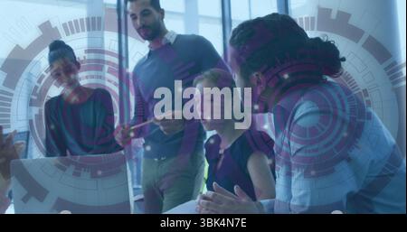 Cinq collègues travaillant autour de l'ordinateur portable sur la table de conférence, avec des documents superposés graphiques Banque D'Images