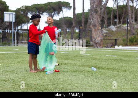 Parc de nettoyage de garçons divers, ramasser des bouteilles en plastique, profiter du travail d'équipe et de la nature Banque D'Images