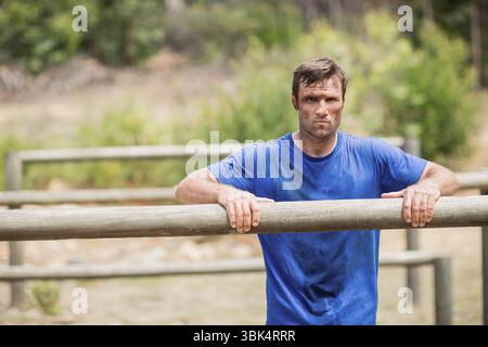 Homme saisissant des poutres en bois tout en s'entraînant sur le parcours d'obstacles dans le défrichement forestier portant une chemise bleue Banque D'Images