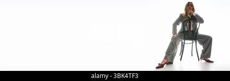 Une jeune femme confiante dans une tenue élégante frappe une pose audacieuse avec une chaise, exsudant le flair de la mode. Banque D'Images