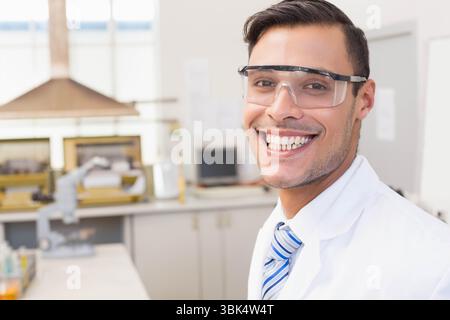 Homme portant une blouse de laboratoire, une cravate rayée et des lunettes de sécurité examinant l'échantillon au microscope sur une paillasse de laboratoire Banque D'Images