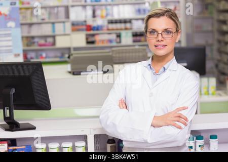 Pharmacienne debout au comptoir de la pharmacie, portant une blouse de laboratoire, face à l'ordinateur et aux bouteilles Banque D'Images