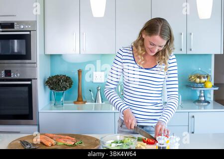 Femme hachant des carottes et du poivron rouge avec couteau de chef sur le comptoir dans la cuisine, espace de copie Banque D'Images